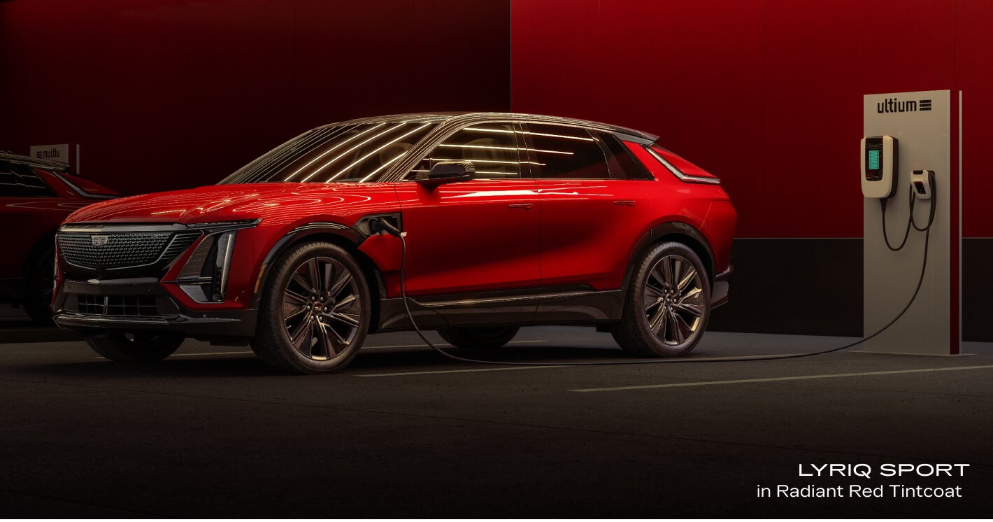 Profile view of a Cadillac LYRIQ Sport in Radiant Red Tintcoat actively charging from a wall-mounted charger station.