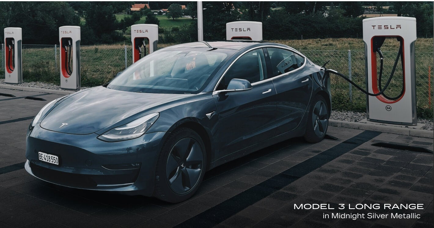 Front-three-quarter view of a Tesla Model 3 Long Range in Midnight Silver Metallic actively charging from a Tesla Supercharger station.