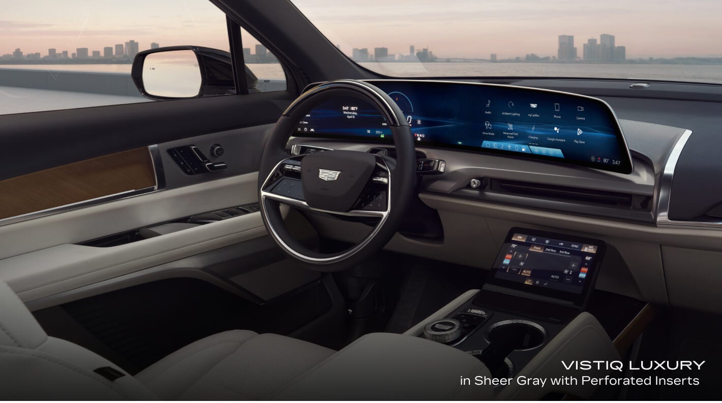 Interior cockpit view of a Cadillac VISTIQ Luxury in Sheer Gray with Perforated Inserts showcasing the steering wheel and curved digital displays.