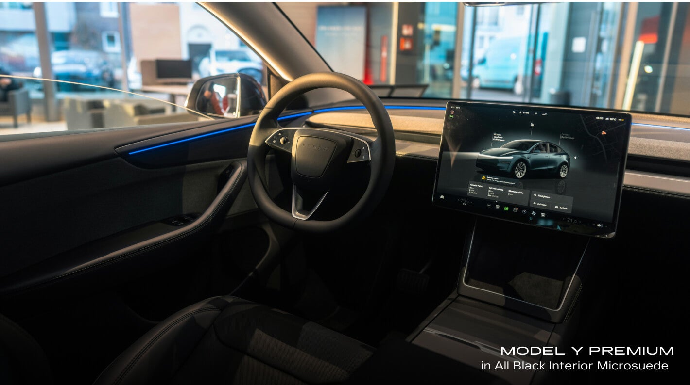 Interior cockpit view of a Tesla Model Y Premium in All Black Interior Microsuede showcasing the steering wheel and center touchscreen display.