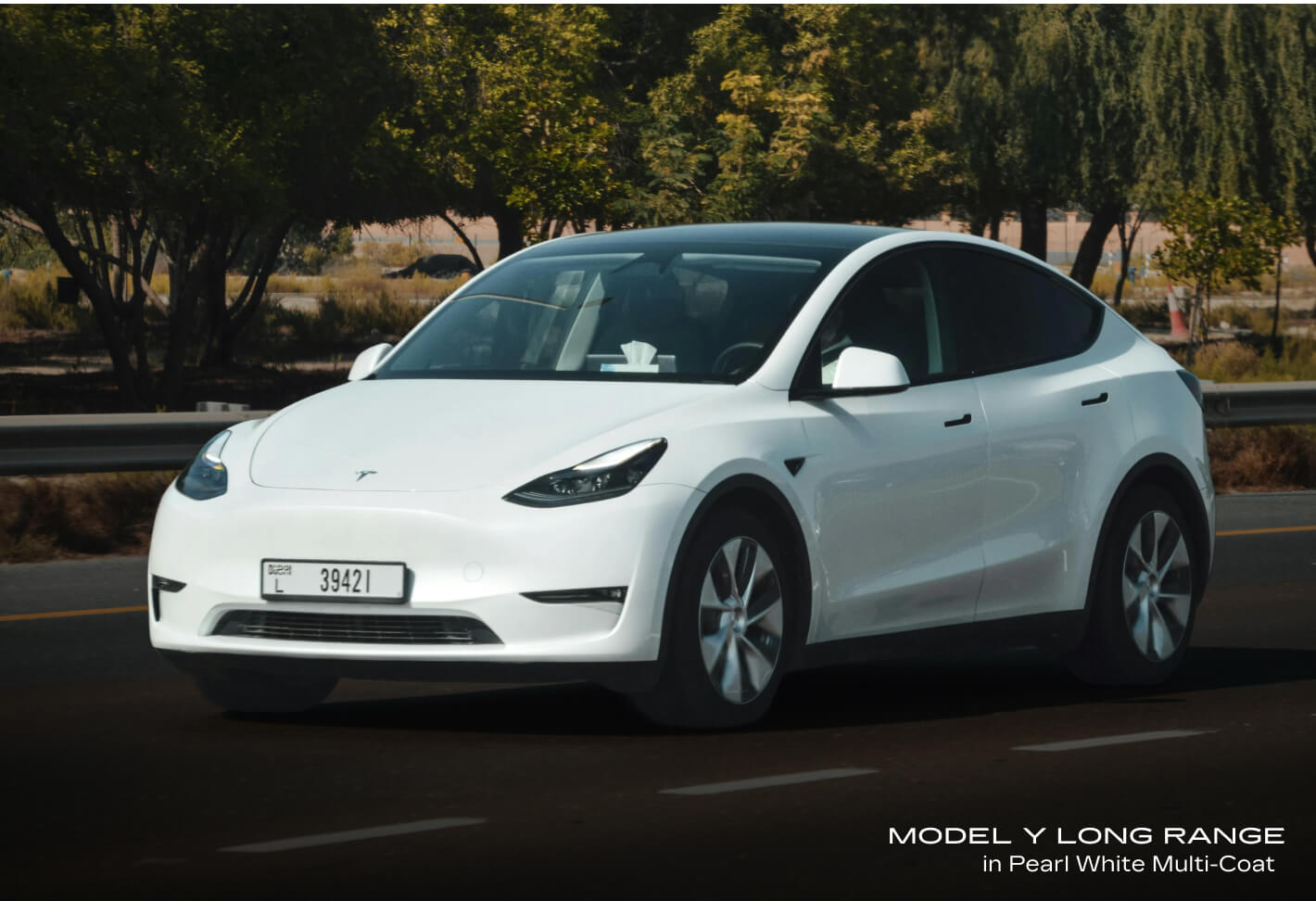 Front-three-quarter view of a Tesla Model Y Long Range in Pearl White Multi-Coat driving on an asphalt road.