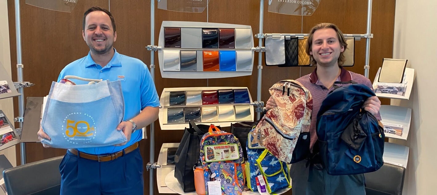 Two members of the Devoe Cadillac team smile while holding donations from a school supply drive.