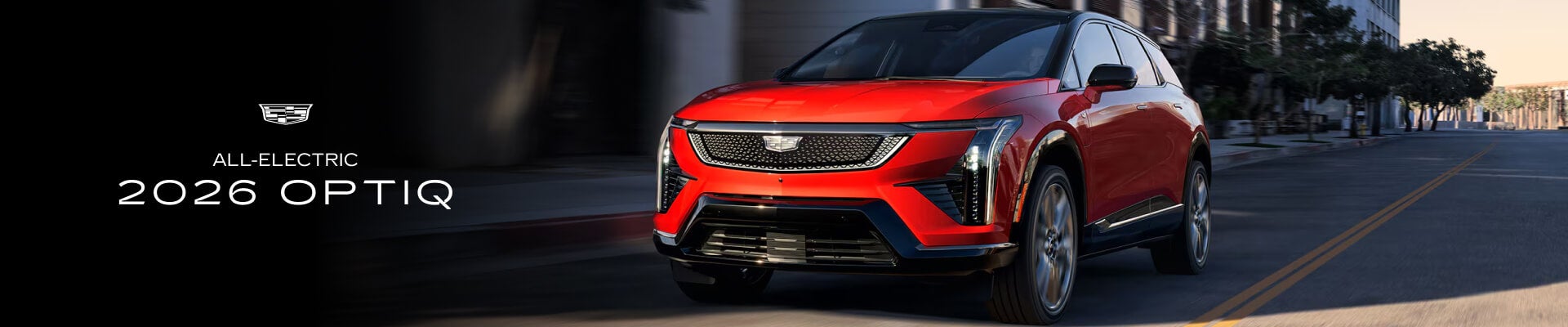 A front view of a red All-Electric 2026 Cadillac OPTIQ driving down a city street.