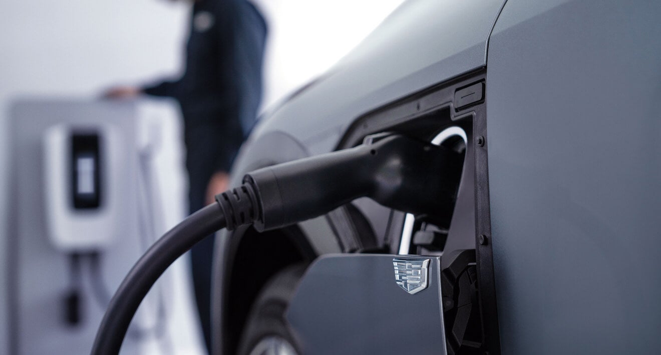 Cadillac Service Technician servicing a charging station with a Cadillac charging port in the foreground