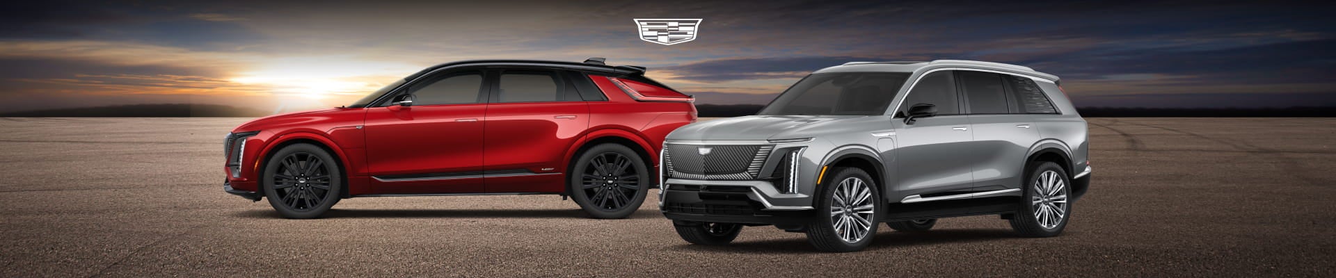 Red and silver Cadillac SUVs displayed side by side against a sunset backdrop.